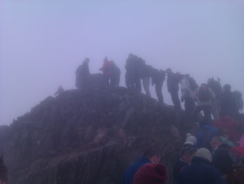 a crowd of walkers at a misty Snowdon summit